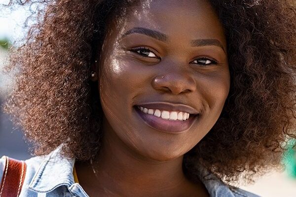 Portrait of young african american woman with curly hair smiling and looking at camera. Black curvy girl in casual clothes enjoying outdoor. Pretty black college student in campus.