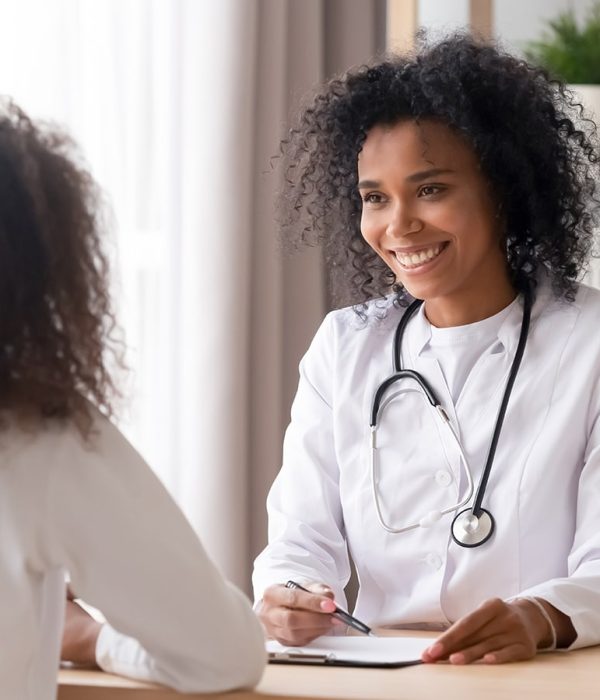Smiling african american female doctor talking to teen patient making notes in clipboard listening to black kid school teenage girl tell complaints fill form at medical clinic checkup appointment.